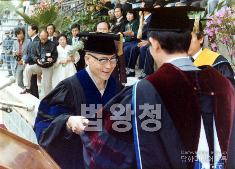 이 사진은 <strong>초대법왕 일붕 서경보 큰스님께서 박사학위를 수여받는 역사적인 순간</strong>을 담고 있습니다. 학위복을 갖춰 입은 큰스님께서 단상 위에서 교수진으로부터 박사 학위를 직접 수여받고 있으며, 환한 미소 속에서 <strong>한국 불교의 위상과 지성의 결실</strong>을 보여주고 있습니다.
