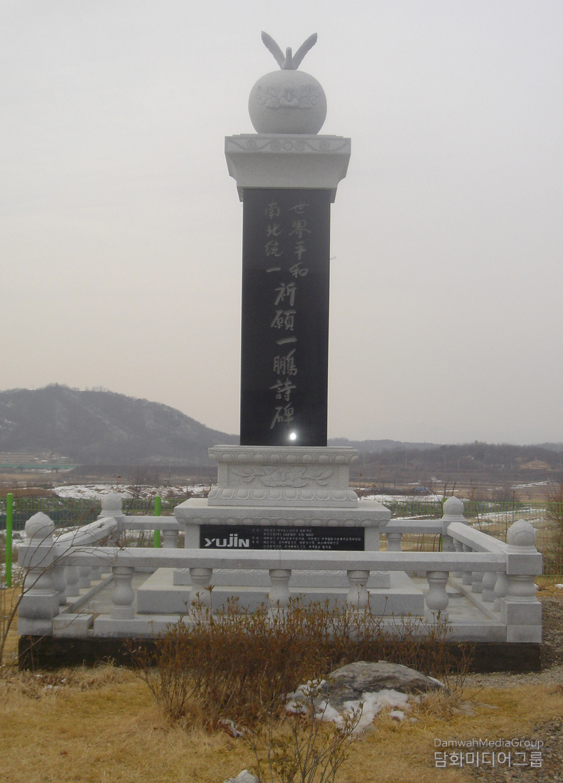 이 사진은 초대법왕 일붕 서경보一鵬 徐京保큰스님께서 생전에 남기신 마지막 통일기원시비, 즉 제787번째 세계평화·남북통일 기원시비의 모습입니다. 경기도 파주시 임진각 통일촌 마을, 북녘이 바라다보이는 민통선 안쪽 최북단 지역 중 하나로, 통일 염원을 상징하는 장소입니다. 1996년 6월 25일, 이 날은 서경보 법왕께서 입적하신 바로 그날로, 이 시비는 열반을 앞두고 세운 마지막 평화의 유산이자, 자비와 통일의 뜻이 응축된 마지막 붓끝이라 할 수 있습니다. 형식적 상징성: 비신碑身 위에는 평화의 상징인 비둘기와 둥근 지구 조형물이 얹혀 있으며, 이는 “자비로 세상을 감싸 안는 불심의 평화, 통일로 하나되는 세계”를 상징합니다. 석재의 단단함과 비문에 새겨진 시의 간절함이 맞물려, 민족사와 불교사에 길이 남을 상징비가 되었습니다. 법왕님께서 생전 총 787기의 통일기원시비를 전국에 직접 건립하셨으며, 그 중 마지막이자 최북단에 세워진 이 비석은 유일하게 입적일에 맞춰 건립되었습니다.<br>
이 비석은 스님의 평생 소원인 남북통일과 세계평화를 향한 기도를 삶의 마지막 순간까지도 놓지 않으셨음을 보여주는 영적 유산입니다. “내 생명이 다하는 그날까지 통일을 노래하고,통일을 새기며, 통일을 기도하겠다.” -일붕 서경보 법왕-